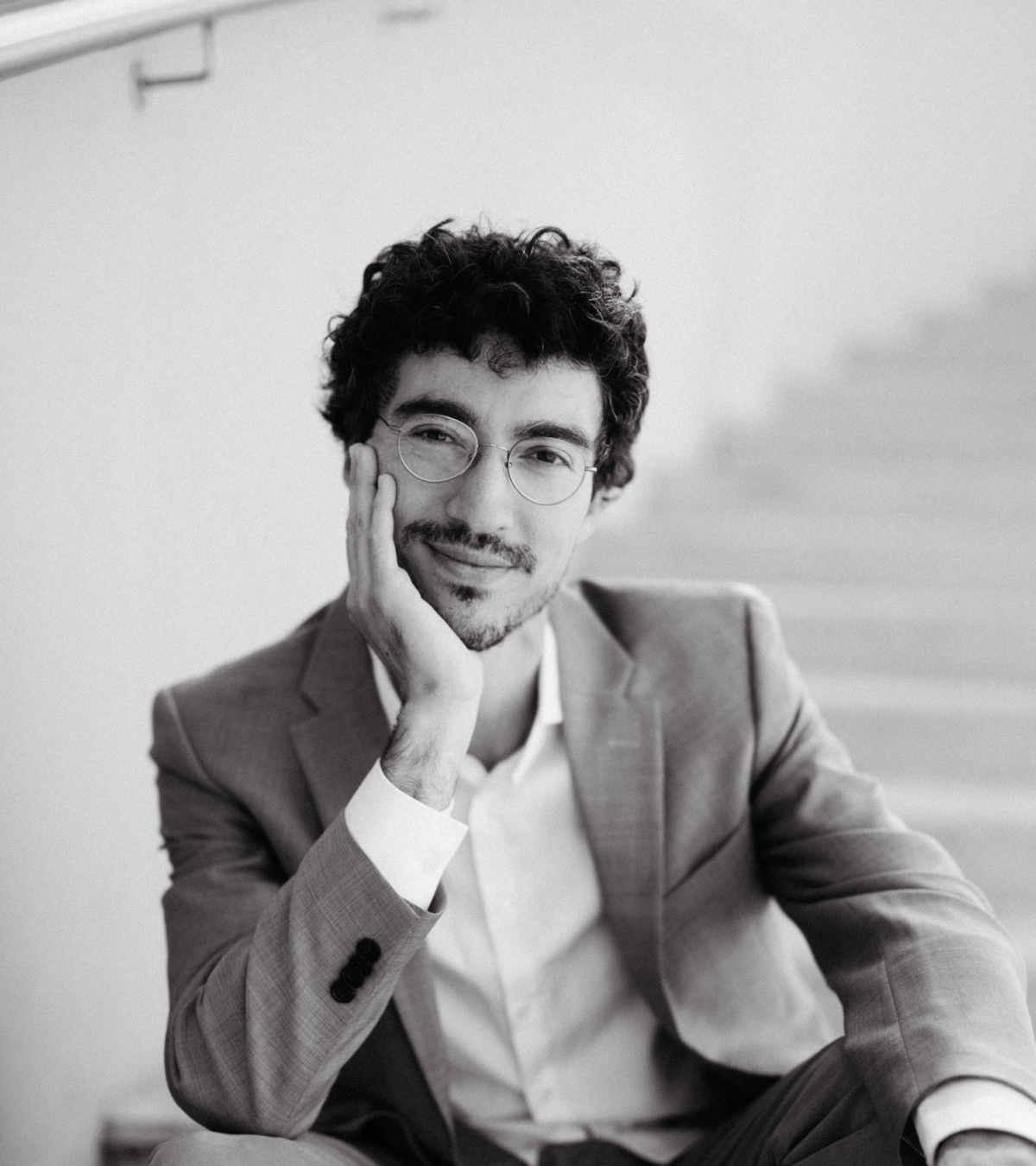 schwarz weiss Foto von Camilo Bornstein, der auf einer Treppe sitzt und sein Gesicht in einer Hand abstützt und in die Kamera lächelt