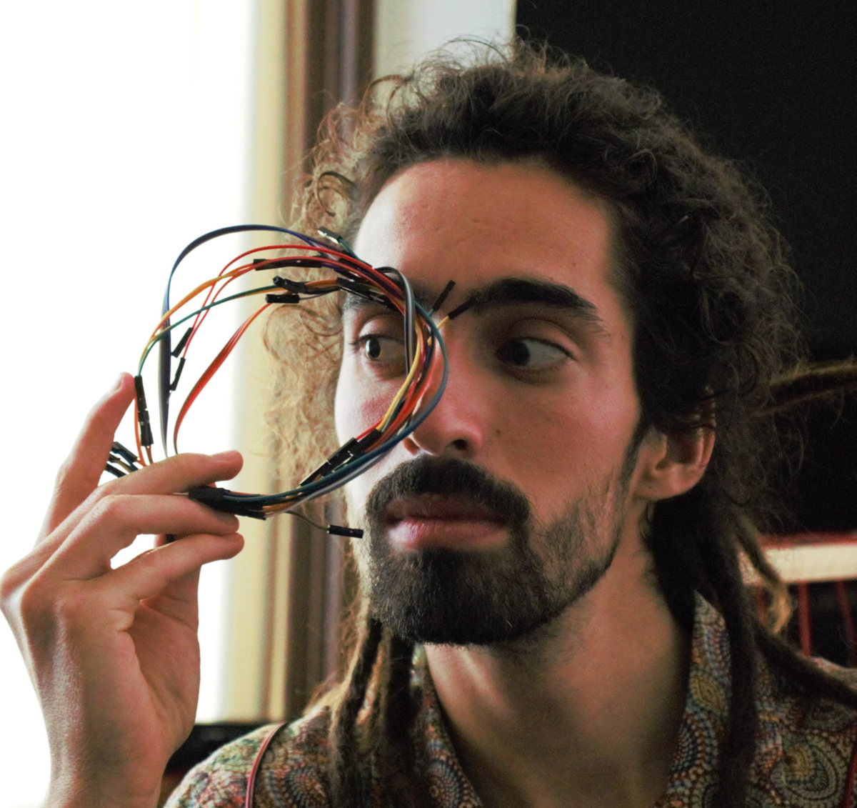 Alexandre Tavares hält sich einen kreis aus Elektrokabeln vor sein eines Auge, durch das er schräg hindurch schaut.