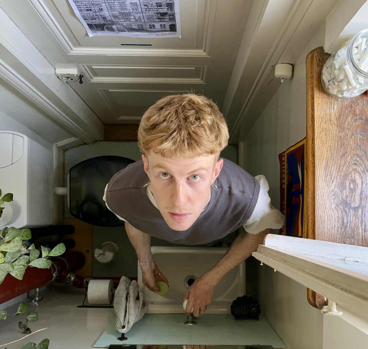 Anton Kiefer wird von oben fotographiert in einer Toilette, vor einem Abwaschbecken stehend und hoch in die Kamera schauend
